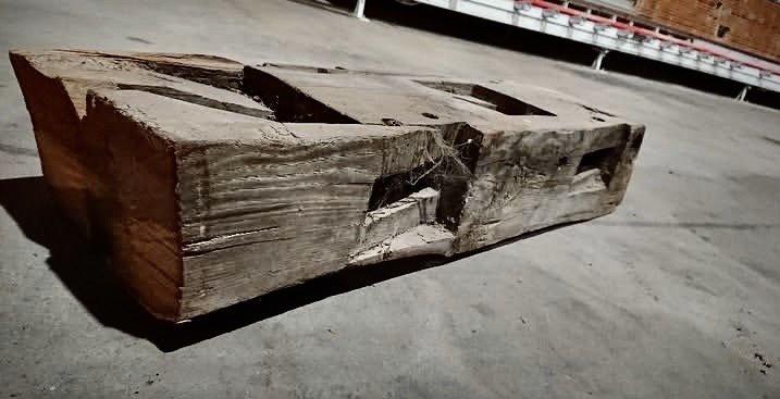 Old hewn beam with empty mortise pockets, lying on concrete
