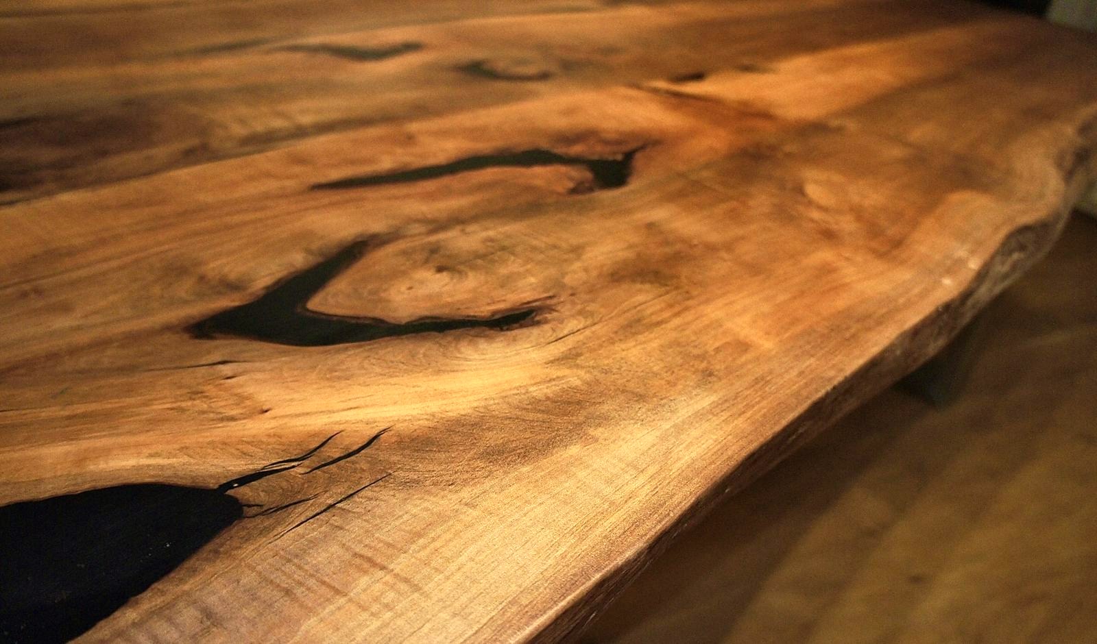 Close view of a salvaged walnut tabletop with black-filled voids and a live edge