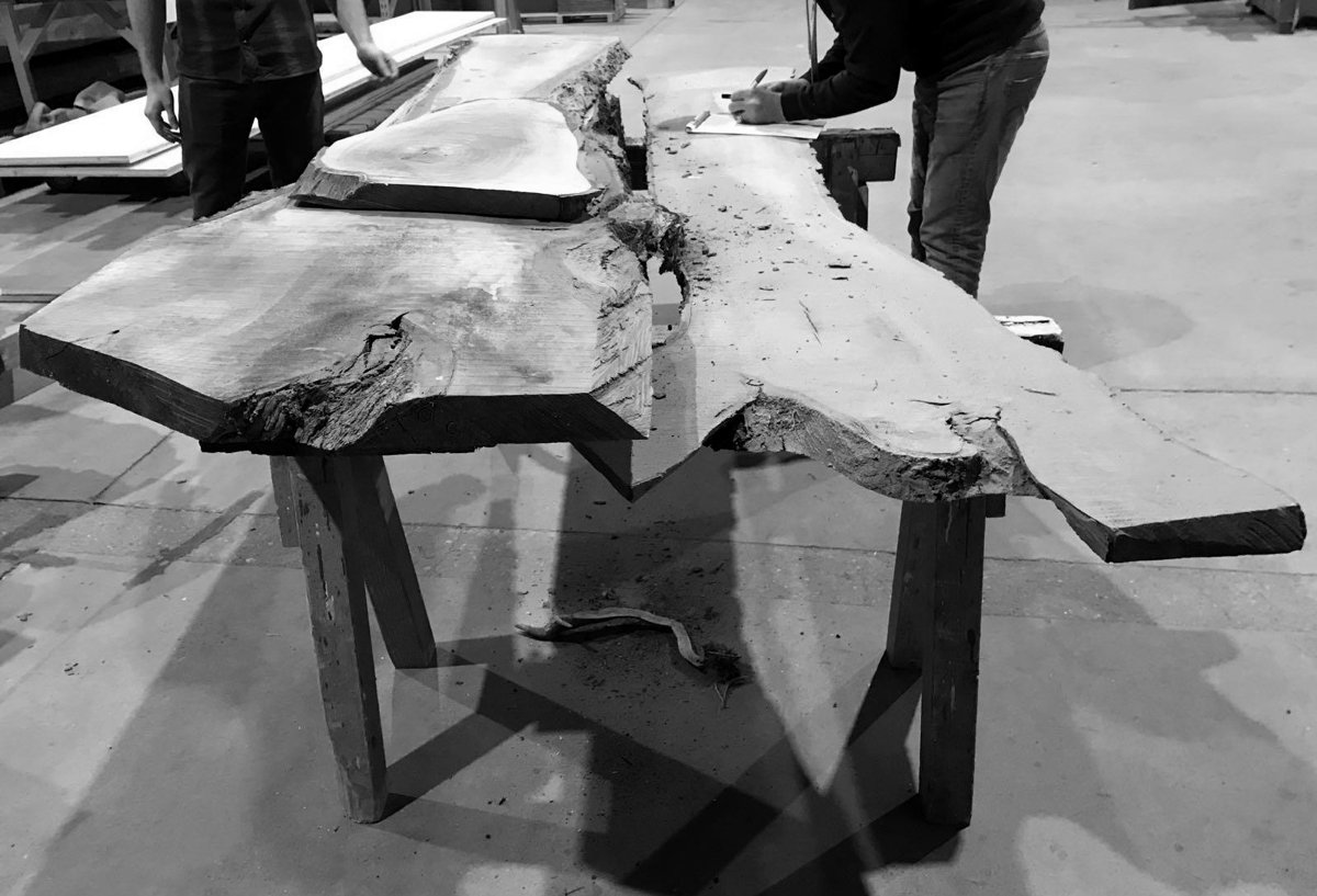 Two people examining live-edge slabs in a timber warehouse, black and white
